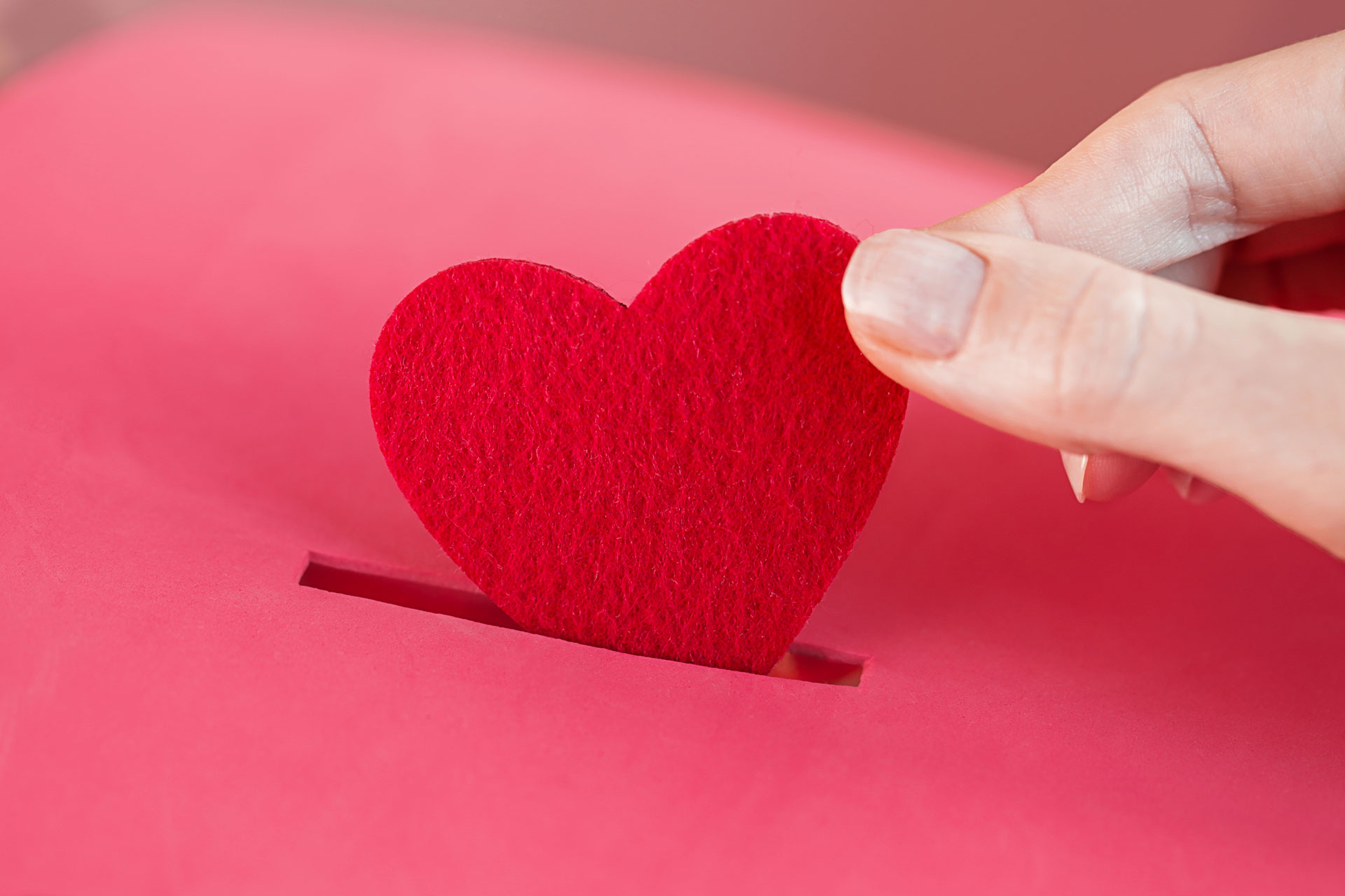 A hand putting a felt heart into a piggy bank.